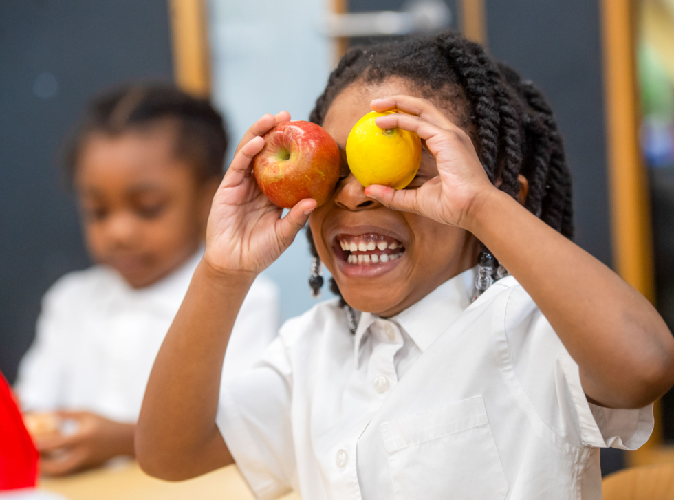 School child holding fruit up to her face