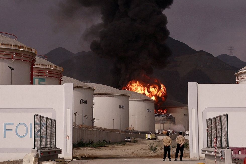 Security guards watch on as an oil facility burns in the UAE after an Iranian strike