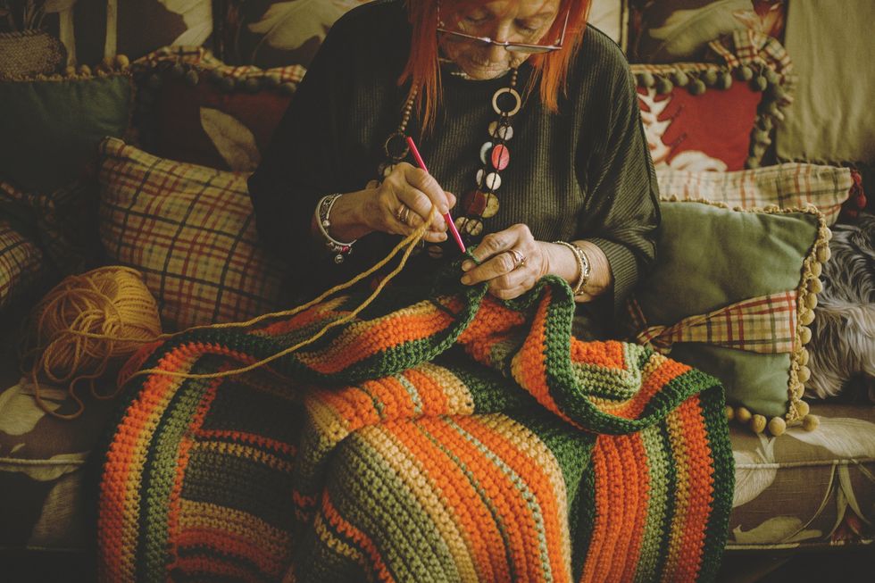 Senior woman crocheting blanket sitting on sofa