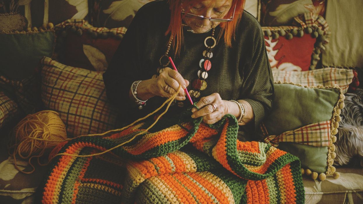 Senior woman crocheting blanket sitting on sofa