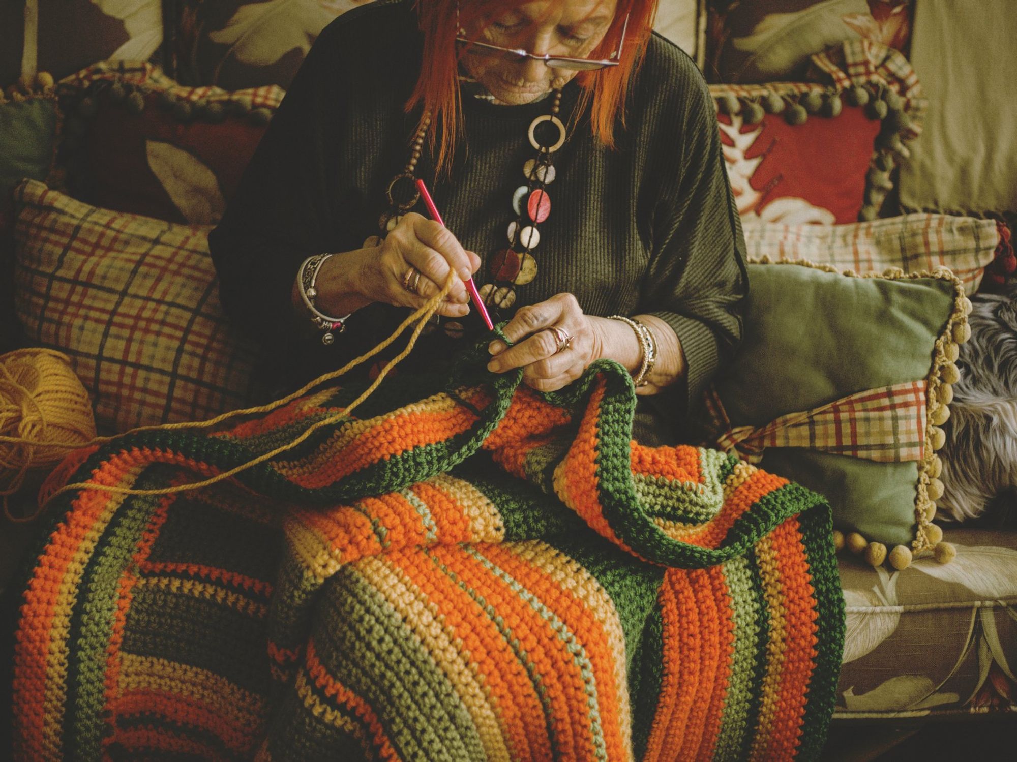 Senior woman crocheting blanket sitting on sofa