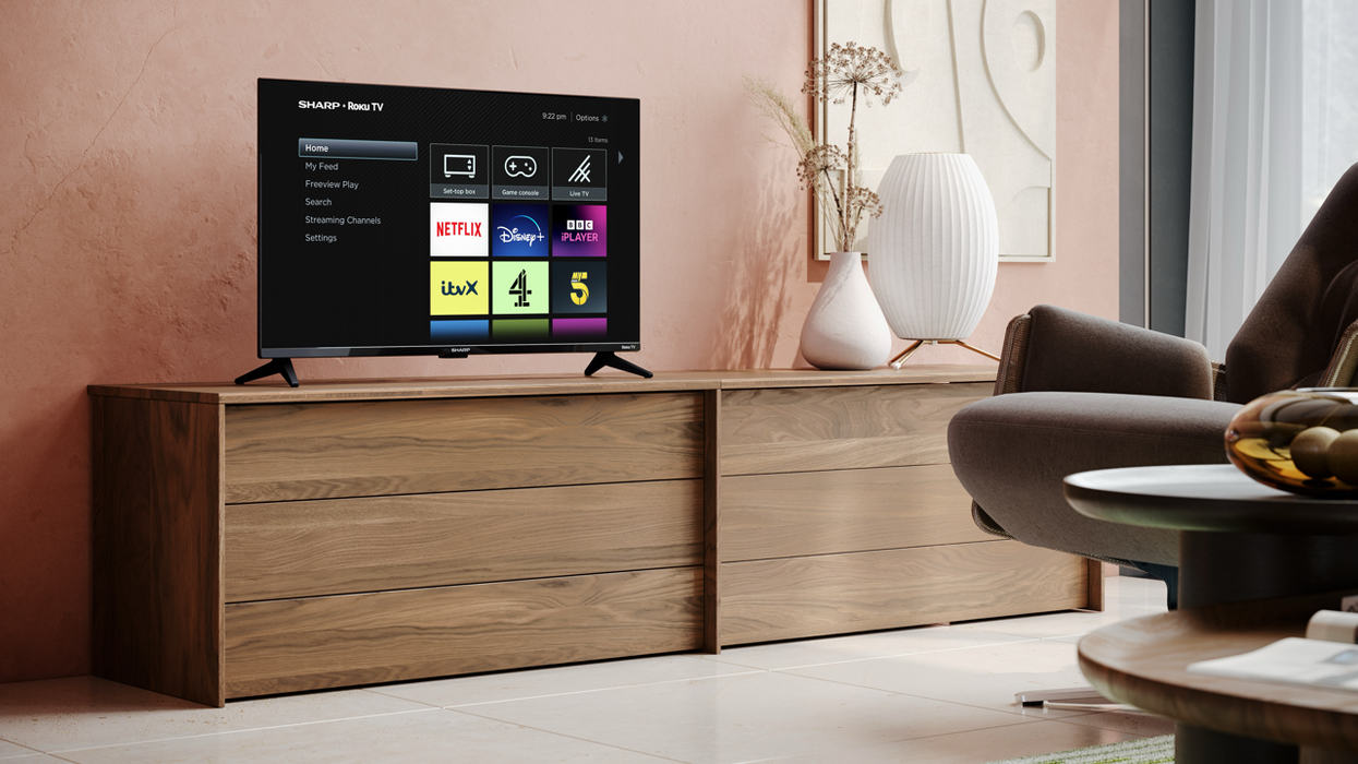 Sharp TV pictured in the corner of a living room with a Roku TV running its software