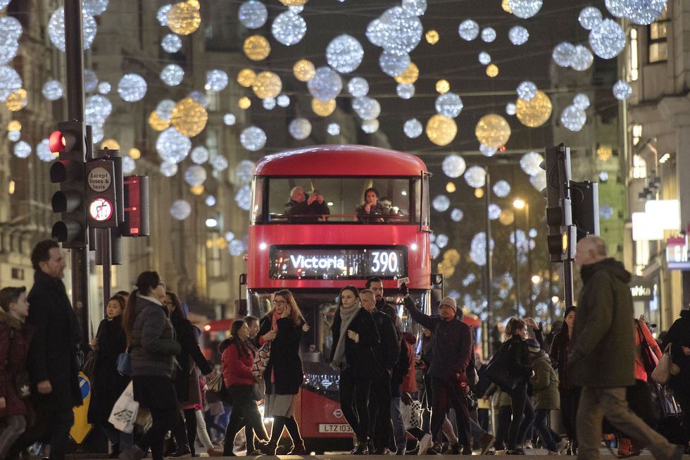 Shoppers cross in front of a London bus as it travels under Christmas lights on Oxford Street
