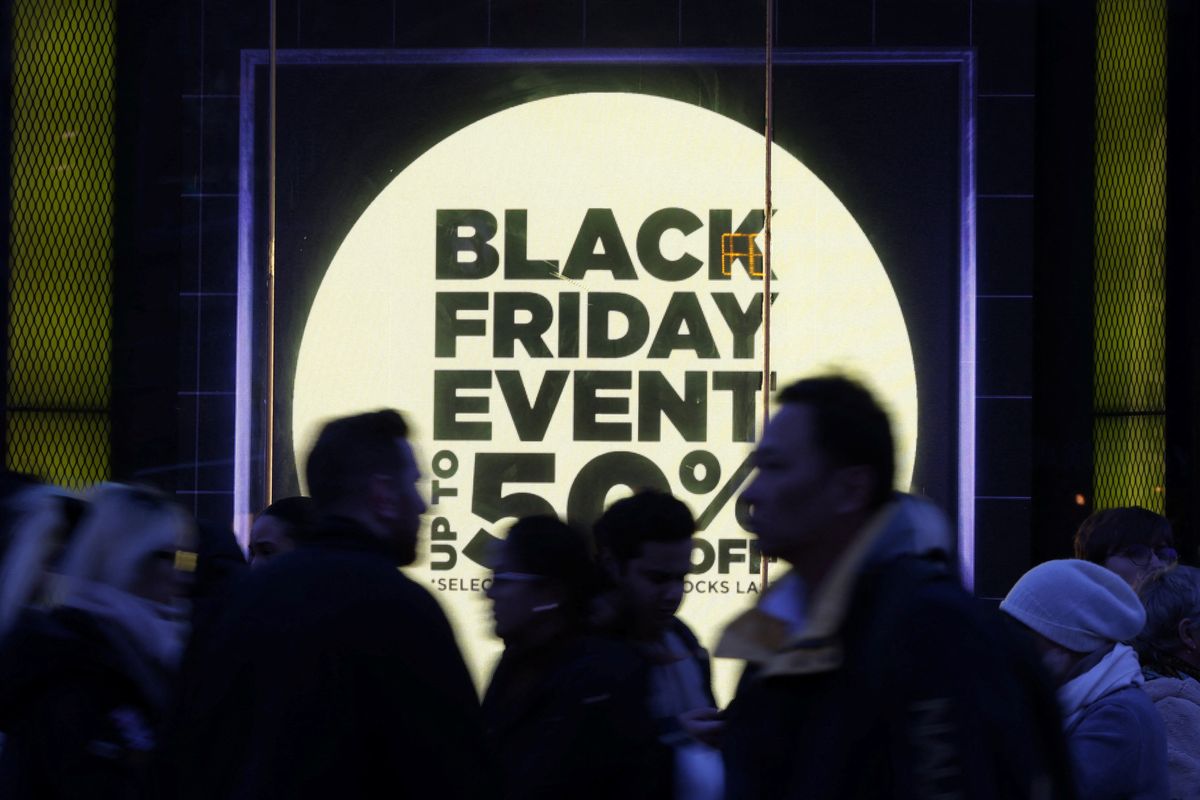 shoppers walk past a store window with a sign promoting the black friday sales 