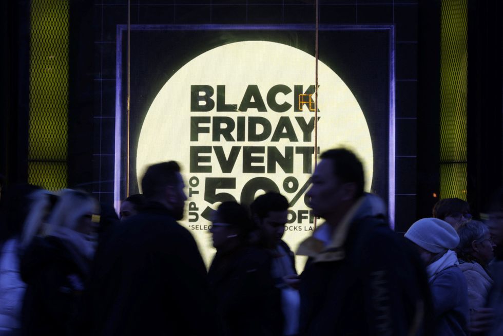 shoppers walk past a store window with a sign promoting the black friday sales
