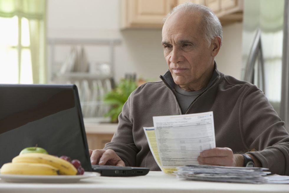 Single pensioner looks serious at laptop beside pension statements
