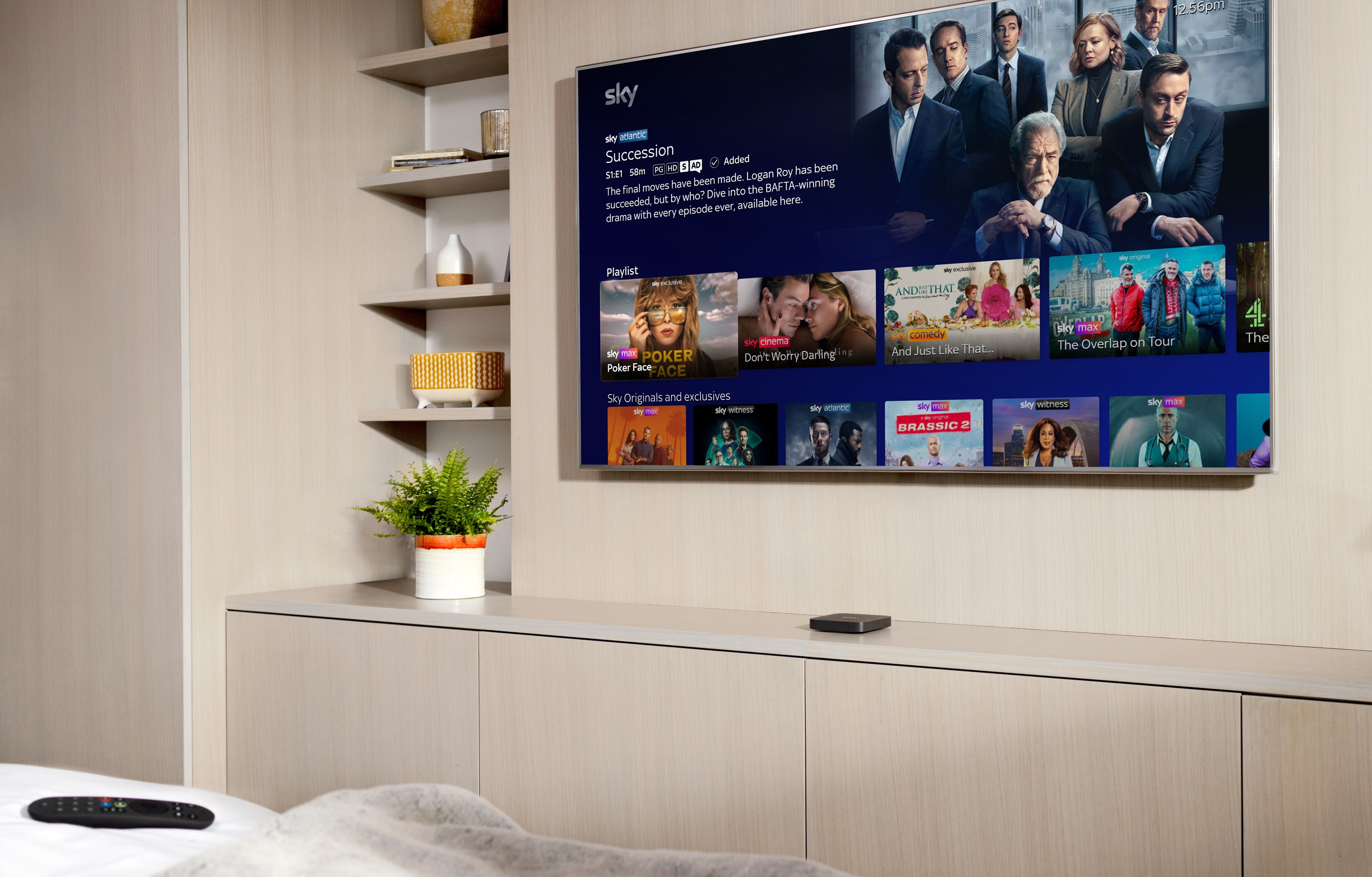 sky stream box pictured on a cabinet underneath a flatscreen television with the remote control lying on a bed