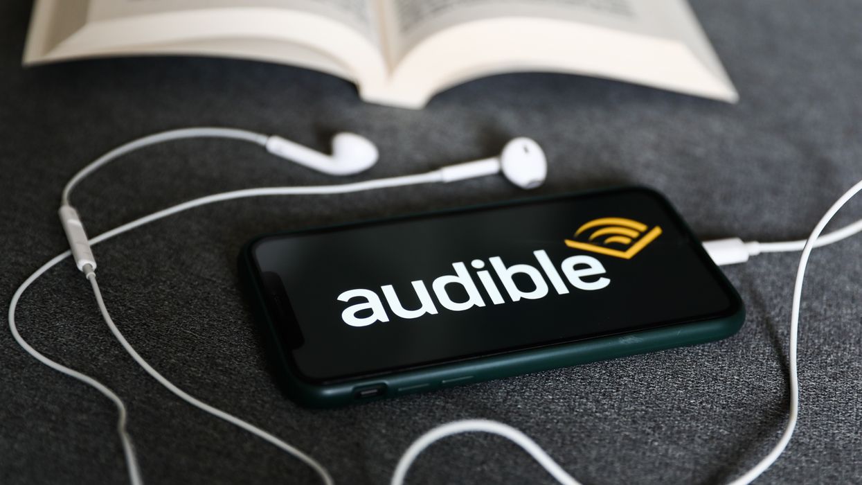 smartphone pictured with the audible app running next to an open book