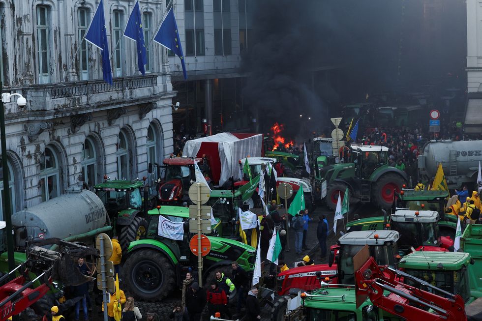 Smoke rises from a fire burning as Belgian farmers use their tractors to block the European Union headquarters
