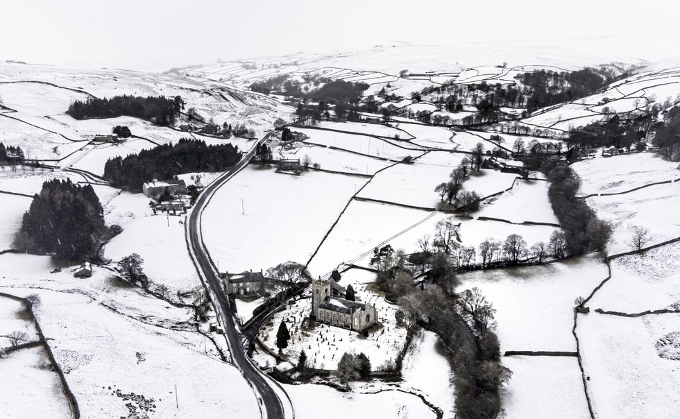 Snow covers fields and hills surround St Mary The Virgin Church in the Arkengarthdale, North Yorkshire.