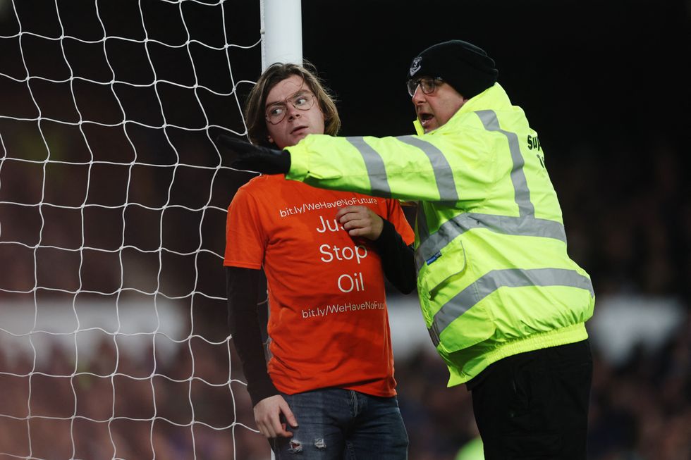 Soccer Football - Premier League - Everton v Newcastle United - Goodison Park, Liverpool, Britain - March 17, 2022 A steward stands next to a protester who tied himself to a goalpost during the match Action Images via Reuters/Lee Smith EDITORIAL USE ONLY. No use with unauthorized audio, video, data, fixture lists, club/league logos or 'live' services. Online in-match use limited to 75 images, no video emulation. No use in betting, games or single club /league/player publications.  Please contact your account representative for further details.