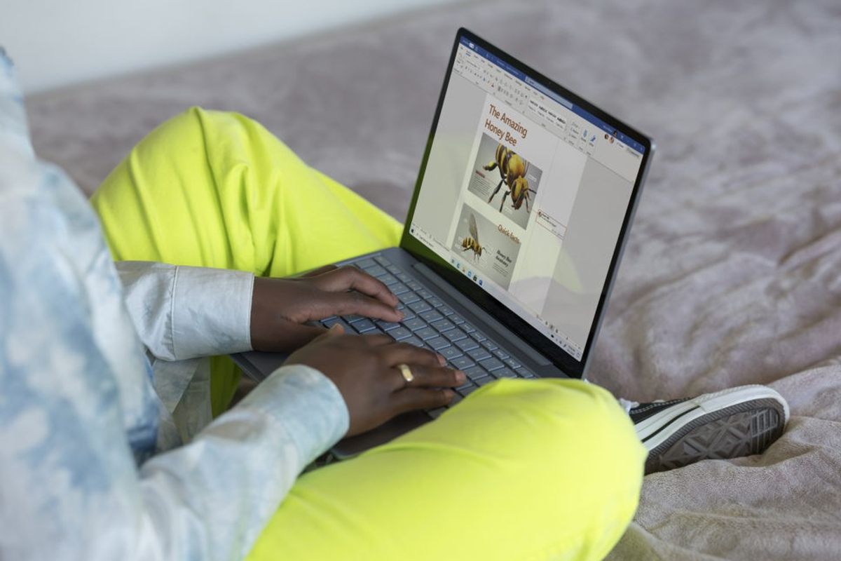 someone is pictured sitting cross-legged with a Microsoft Surface laptop on their lap running Windows