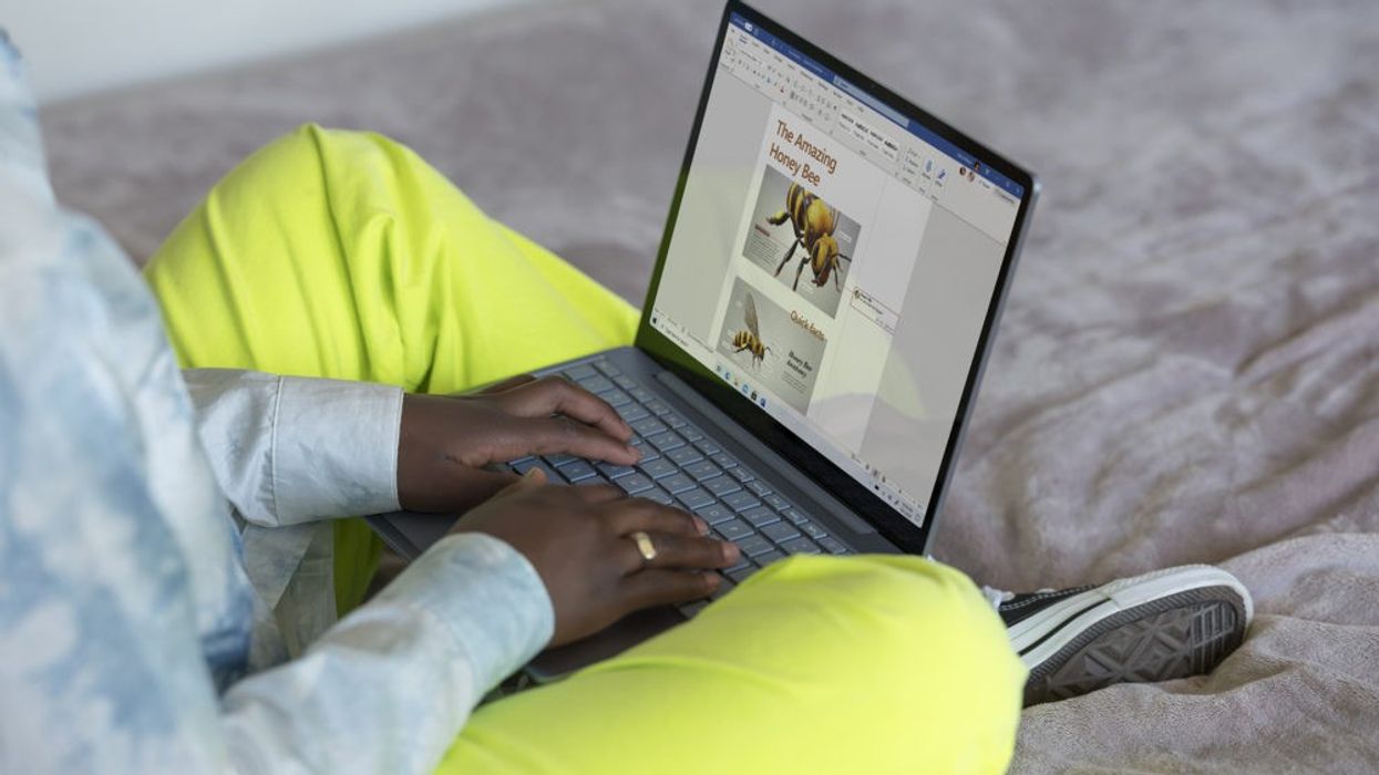 someone is pictured sitting cross-legged with a Microsoft Surface laptop on their lap running Windows