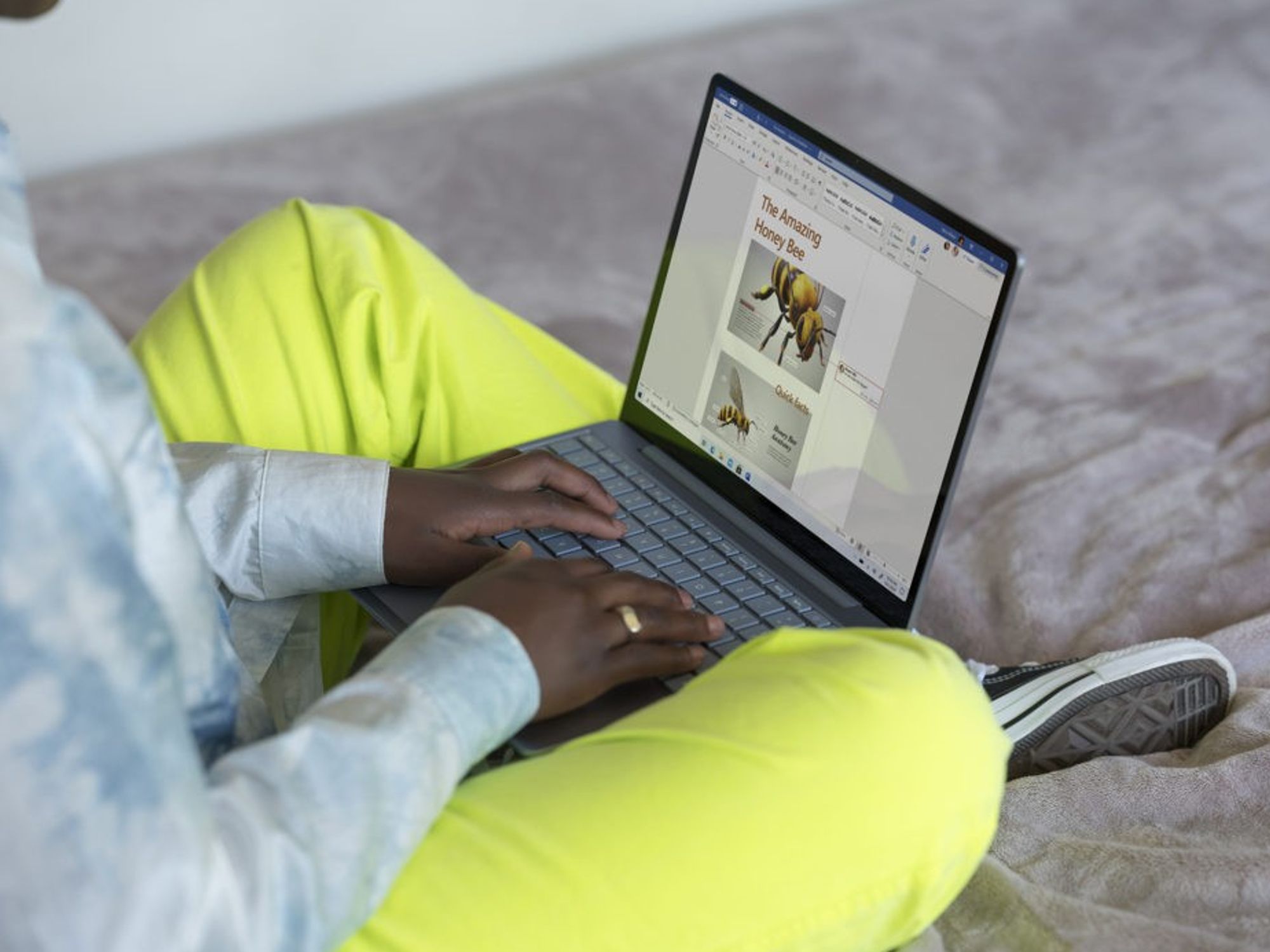 someone is pictured sitting cross-legged with a Microsoft Surface laptop on their lap running Windows