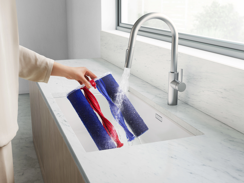someone is pictured washing the microfibre roller heads from the dyson wash g1