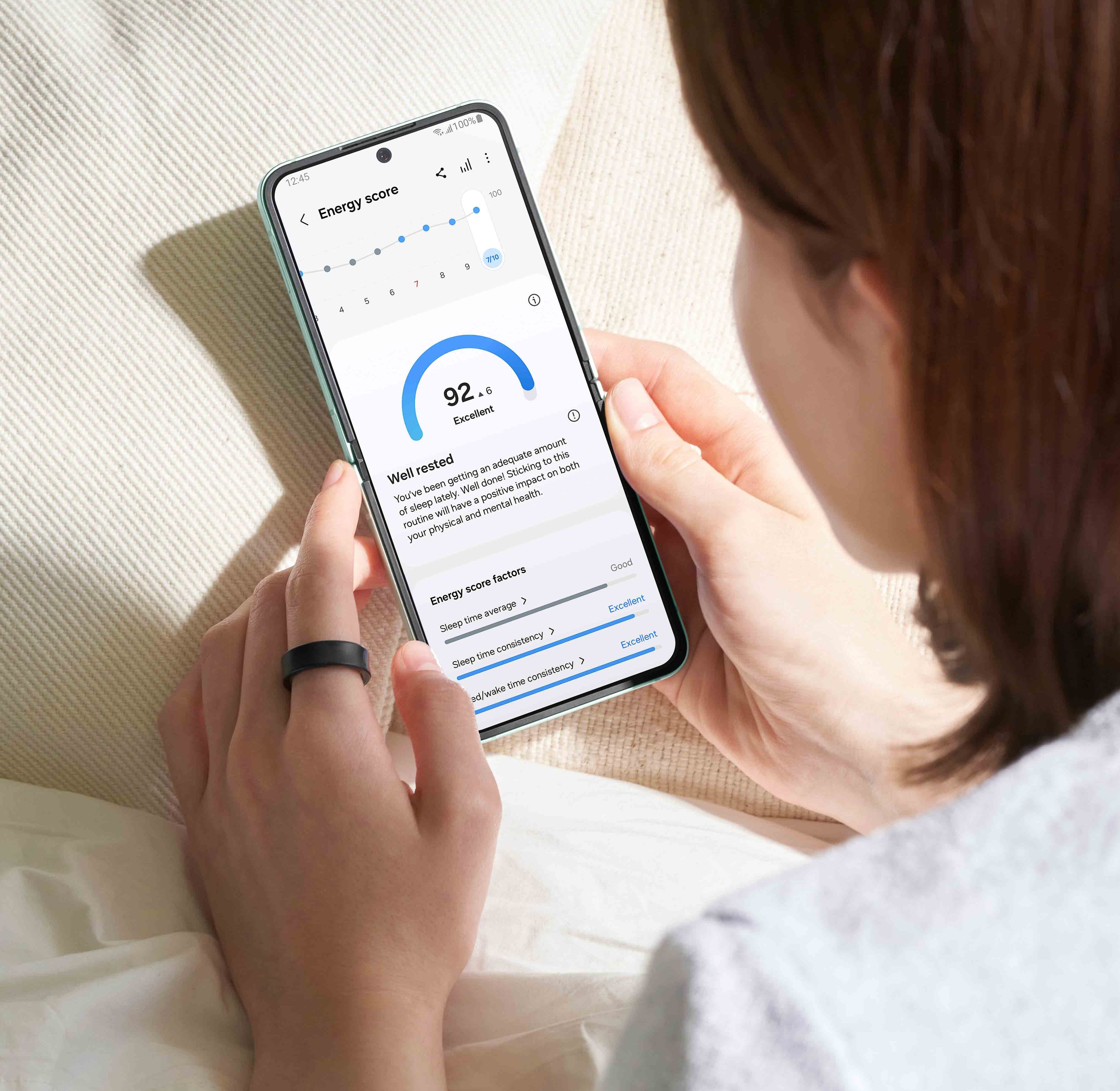 someone lies on a bed checking their energy score on a galaxy z flip 6