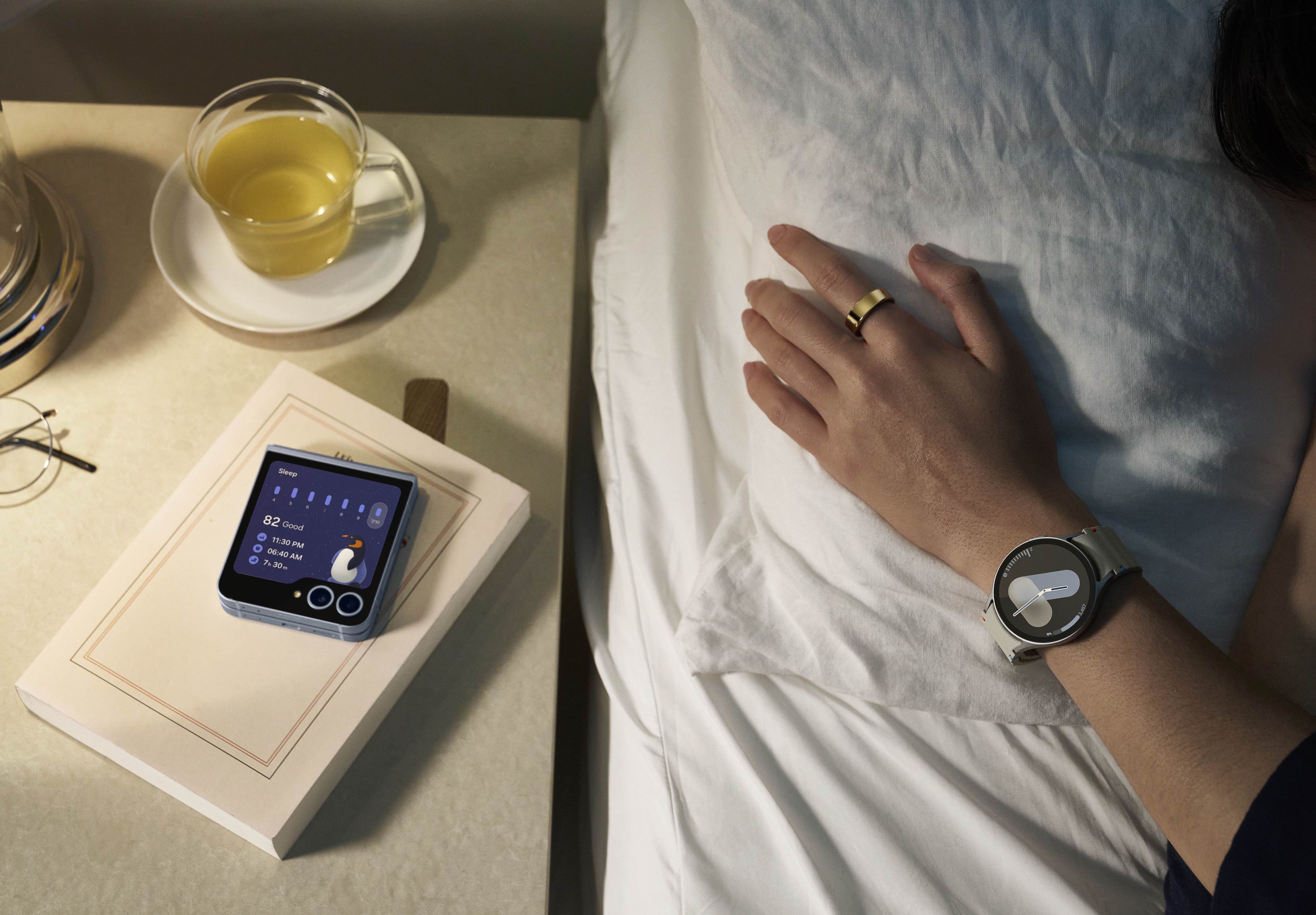 someone lying in bed wearing a galaxy watch 7 with the galaxy z flip 6 on a bedside table