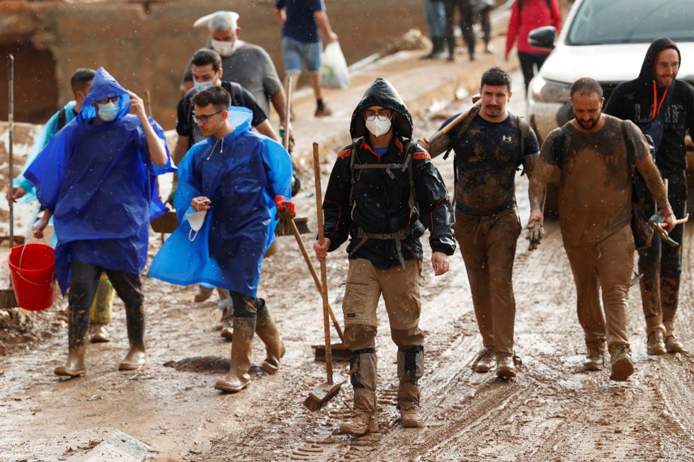 Spain: Clean-up workers walk through muddy streets with brooms