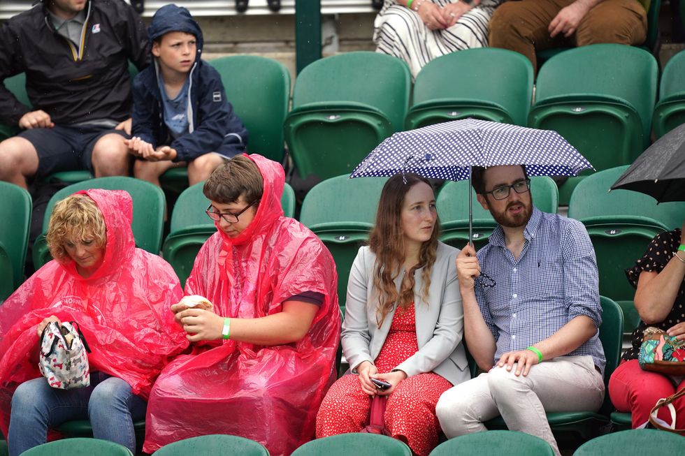Spectators take cover from the rain at Wimbledon