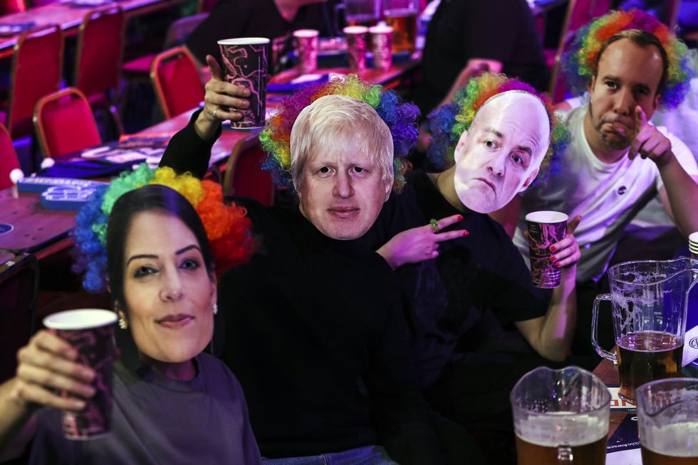 Spectators wear masks that show the faces of Priti Patel, Boris Johnson, Dominic Cummings and Matt Hancock during day two of the William Hill World Darts Championship at Alexandra Palace, London. Picture date: Thursday December 16, 2021.
