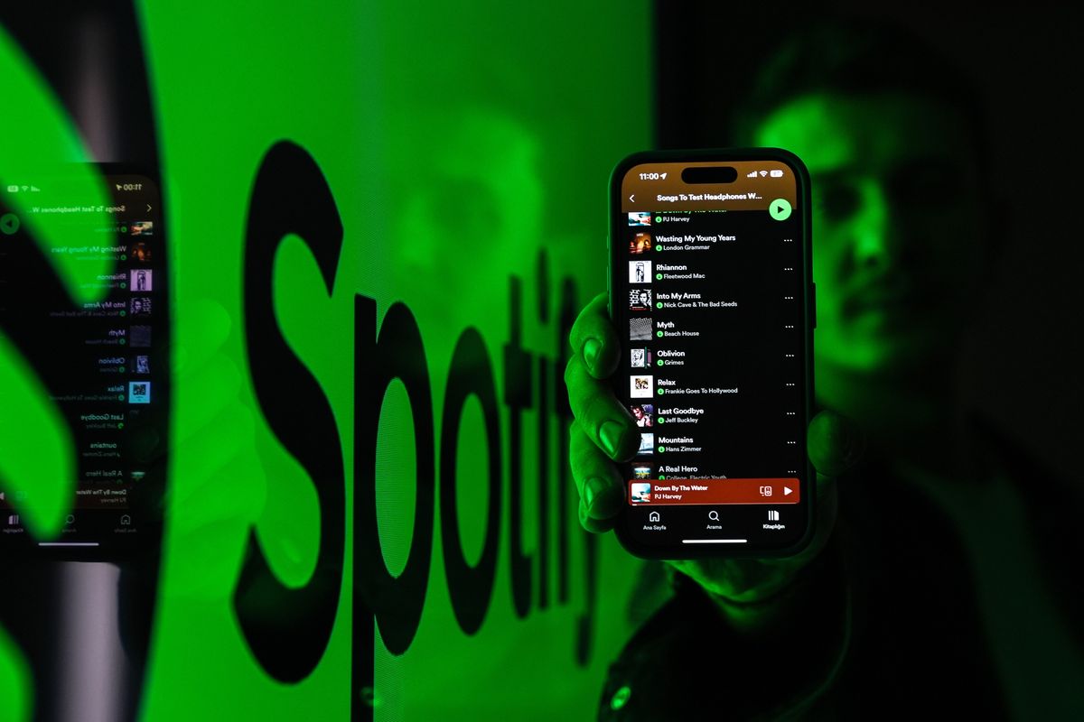 Spotify app open on phone being held by man with logo in the background
