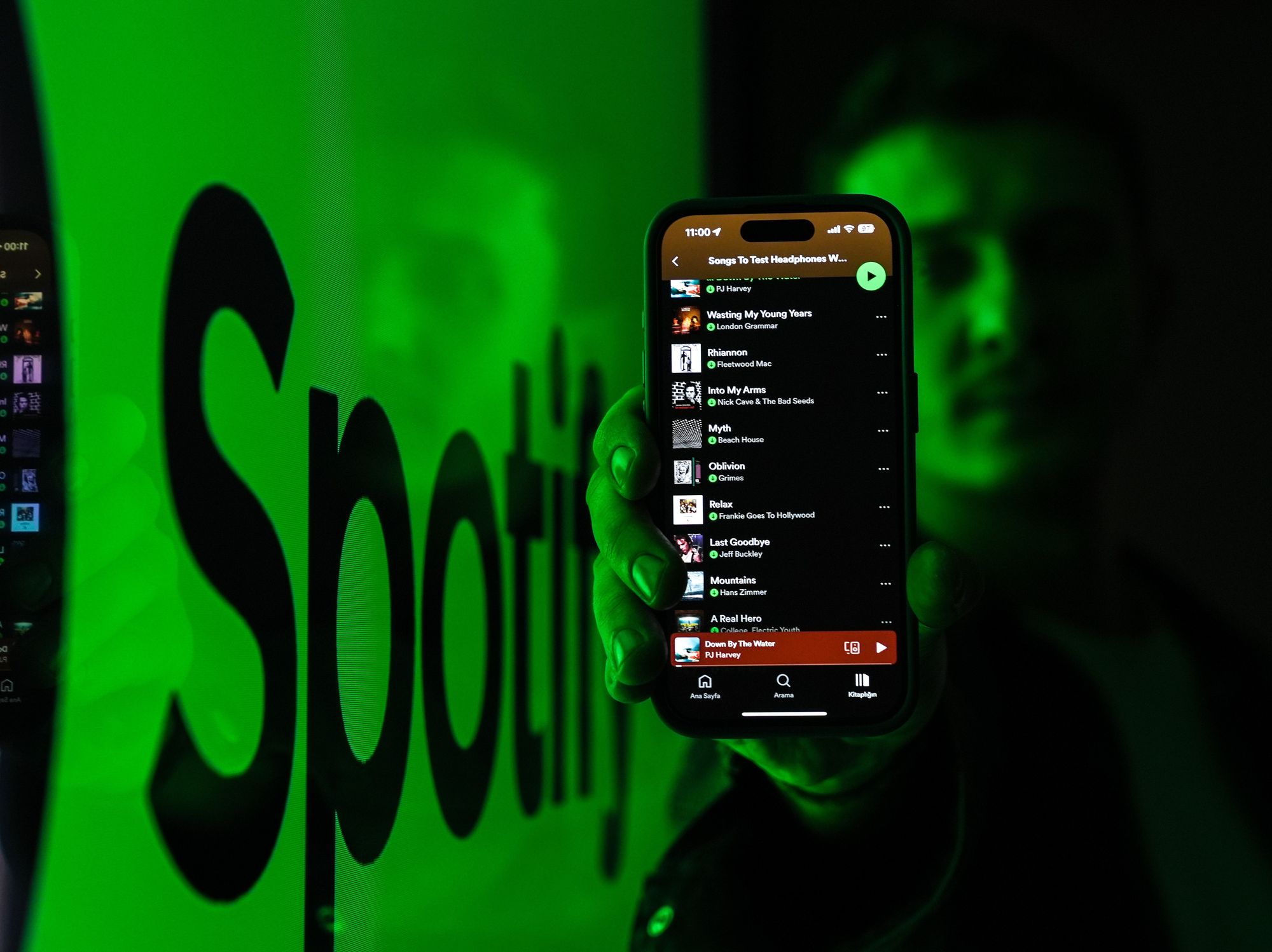 Spotify app open on phone being held by man with logo in the background