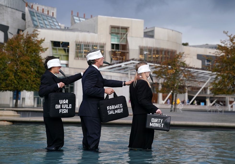 Suited performers from Ocean Rebellion, wearing blindfolds and gagged with dead fish, protest at Holyrood Pond, outside the Scottish Parliament in Edinburgh, calling on Scottish Government to wind down the environmental tragedy of salmon farming with a just transition for workers. Picture date: Friday October 7, 2022.