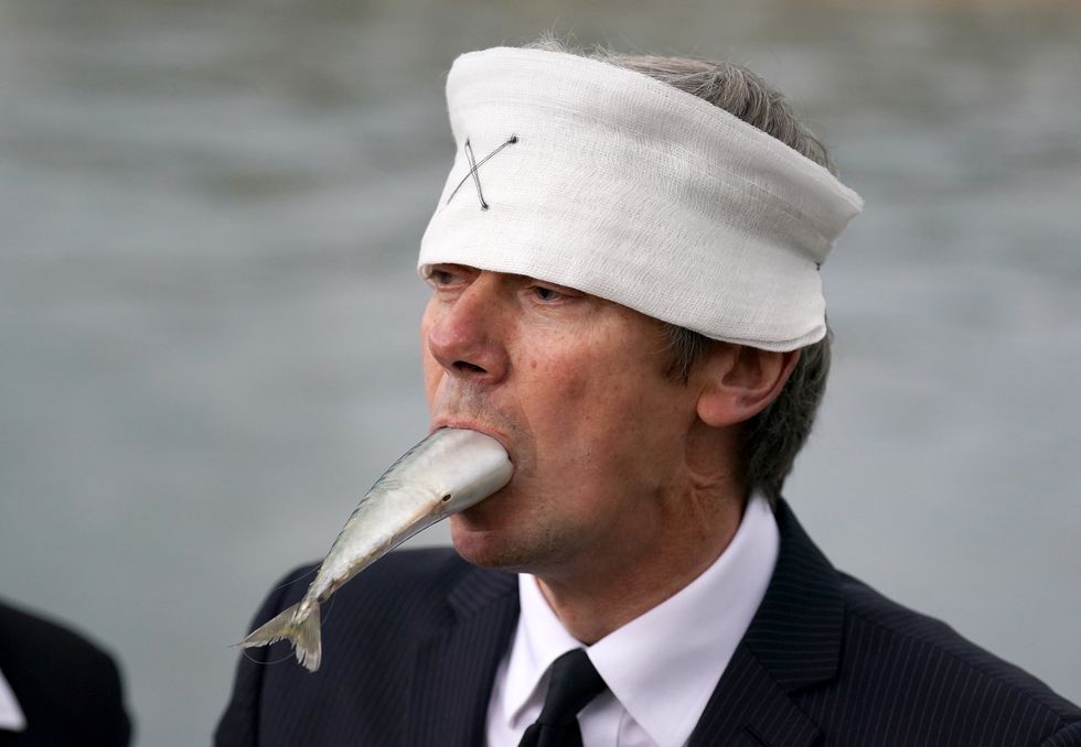 Suited performers from Ocean Rebellion, wearing blindfolds and gagged with dead fish, protest at Holyrood Pond, outside the Scottish Parliament in Edinburgh, calling on Scottish Government to wind down the environmental tragedy of salmon farming with a just transition for workers. Picture date: Friday October 7, 2022.