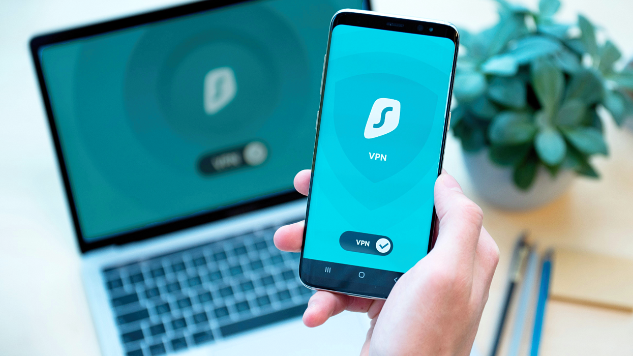 surfshark VPN pictured running on a smartphone screen with a laptop in the background