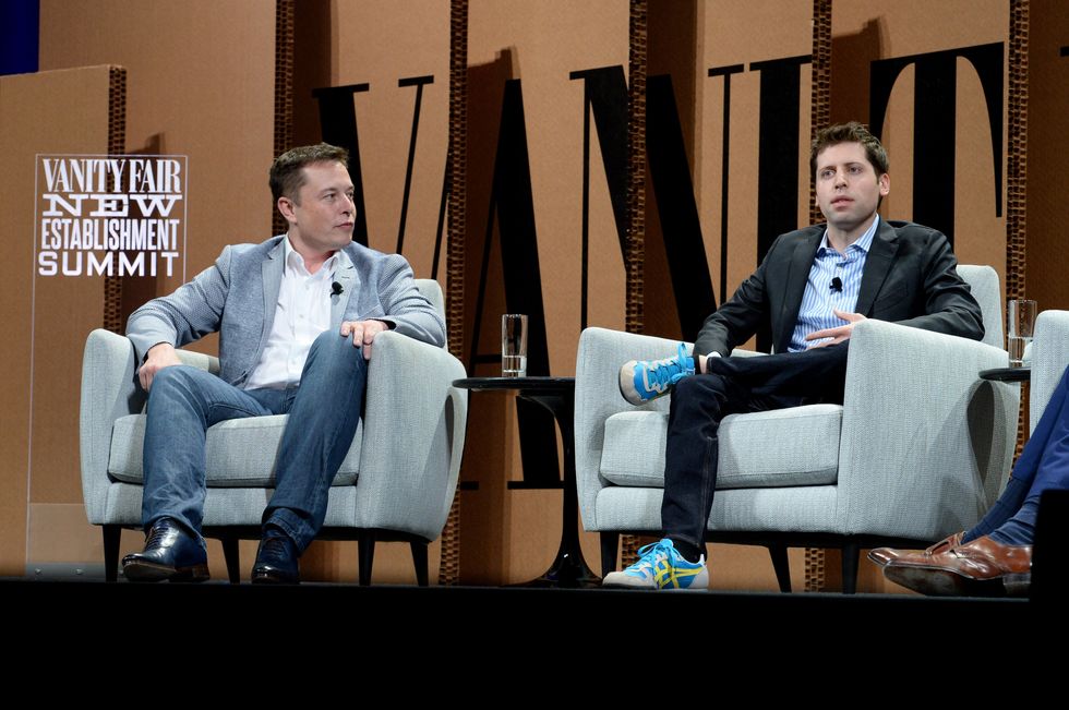 Tesla CEO Elon Musk pictured sitting in a chair on-stage next to OpenAI CEO Sam Altman