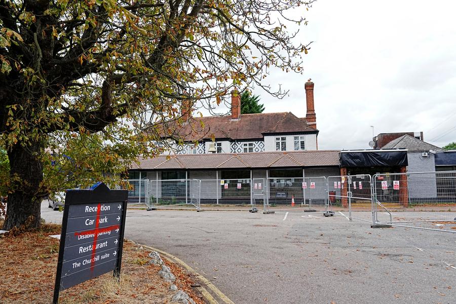 The Bell Hotel in Epping, boarded up with fencing around it. A red cross has been graffitied on the entrance sign.