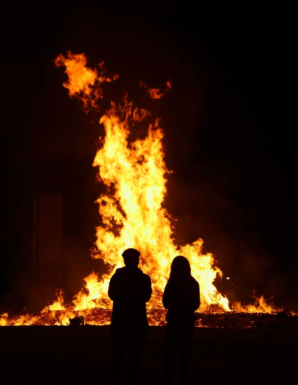 The dismantled bonfire is lit during a vigil where a man died after falling from the bonfire on the Antiville estate in Larne, Co Antrim