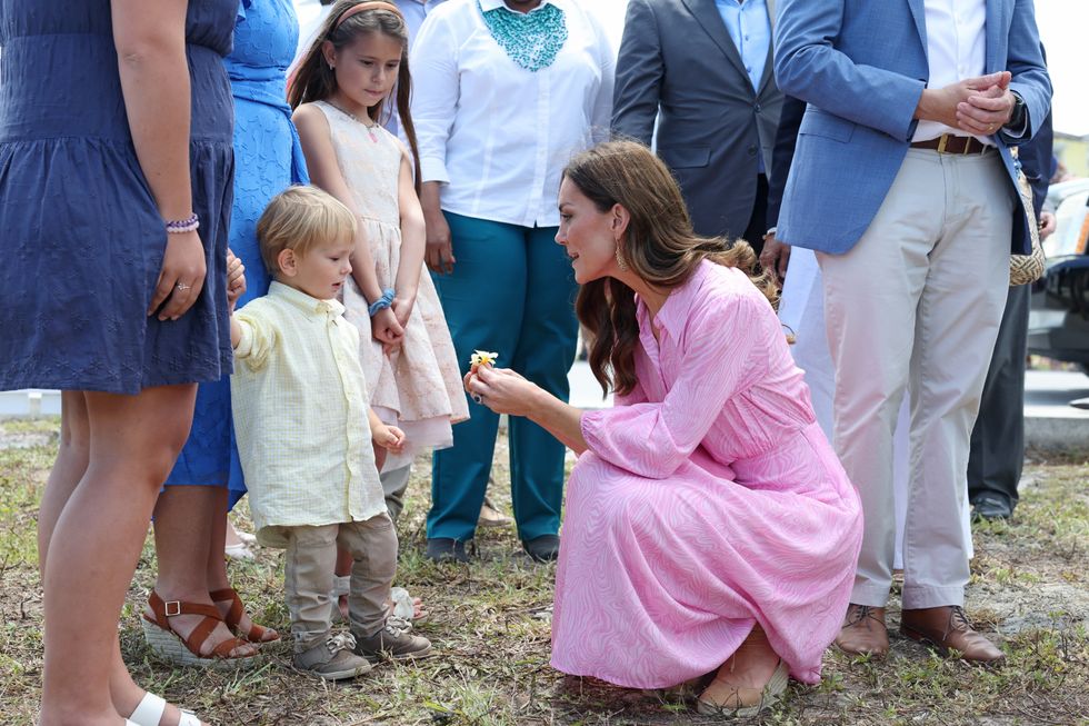 The Duchess of Cambridge picks a flower and speaks with children during a visit to the Memorial Wall to remember victims of the 2019 hurricane at the Memorial Garden in Abaco, on day eight of their tour of the Caribbean on behalf of the Queen to mark her Platinum Jubilee. Abaco, a chain of islands and barrier cays in the northern Bahamas, was hit by winds of up to 185mph during Hurricane Dorian in 2019 leaving 75% of homes across the chain of islands damaged and resulting in tragic loss of life. Picture date: Saturday March 26, 2022.