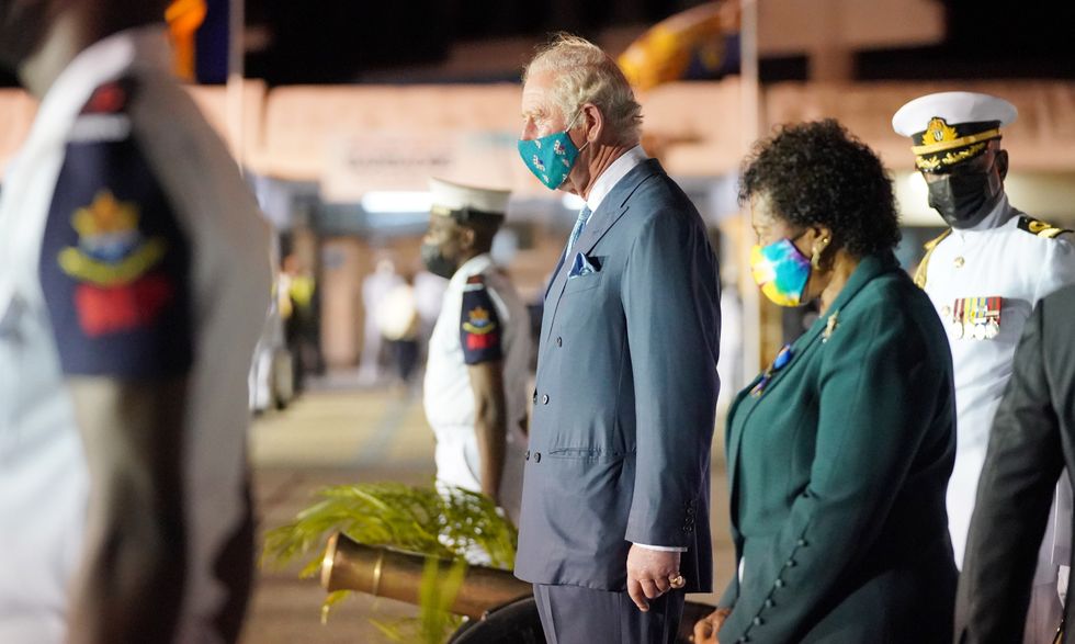 The Prince of Wales observes a gun salute, standing alongside Sandra Mason.