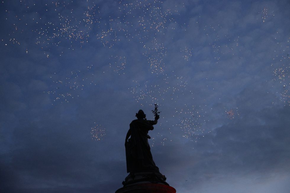 The statue of Marianne is seen among fireworks as people gather at the Place de la Republique