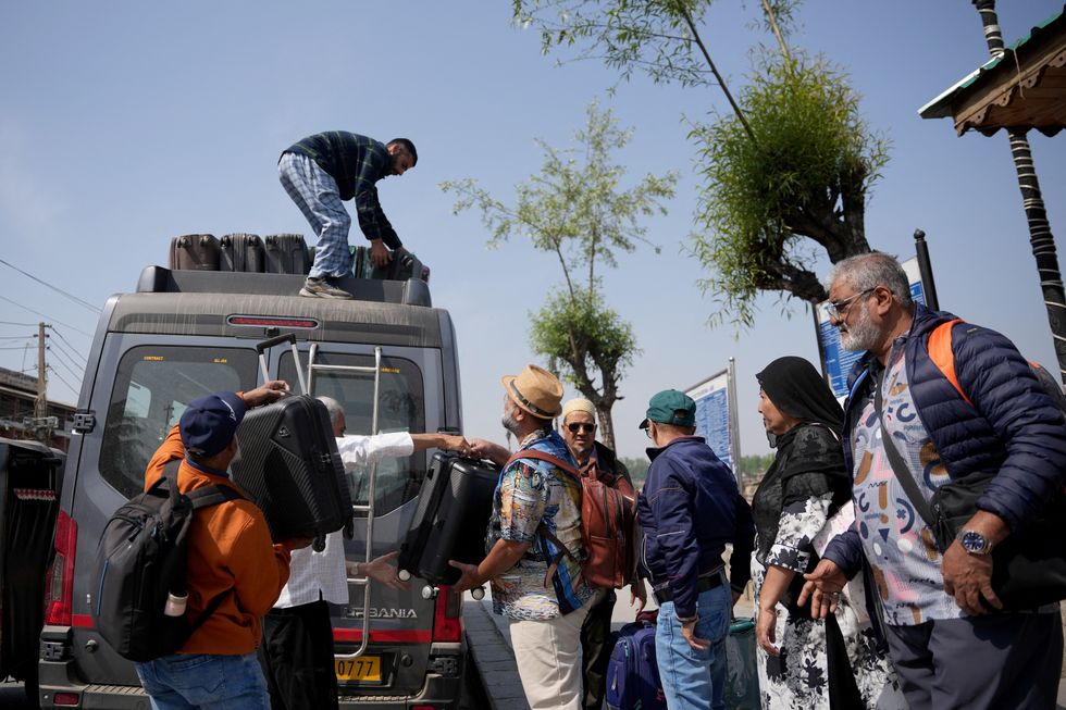 Tourists get their belongings loaded on a vehicle as they leave for Srinagar airport