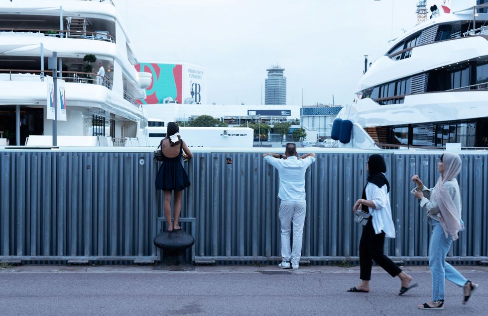Tourists look at yachts on the seafront in Barcelona