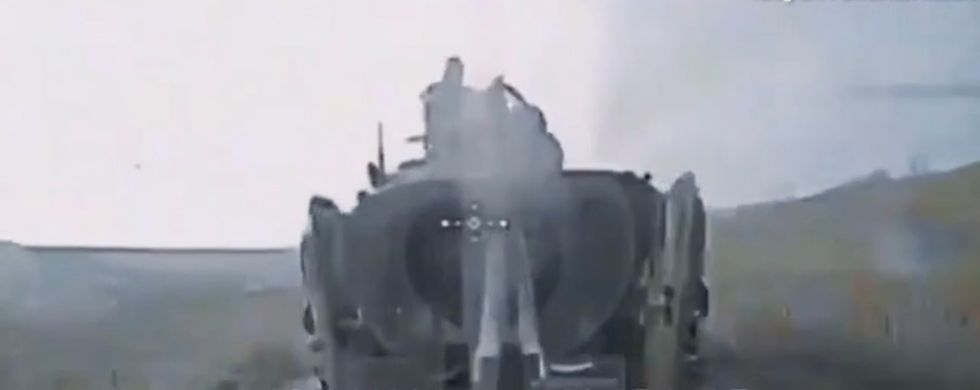 Two men sit on top of the vehicle and appear panicked as the drone gets nearer.