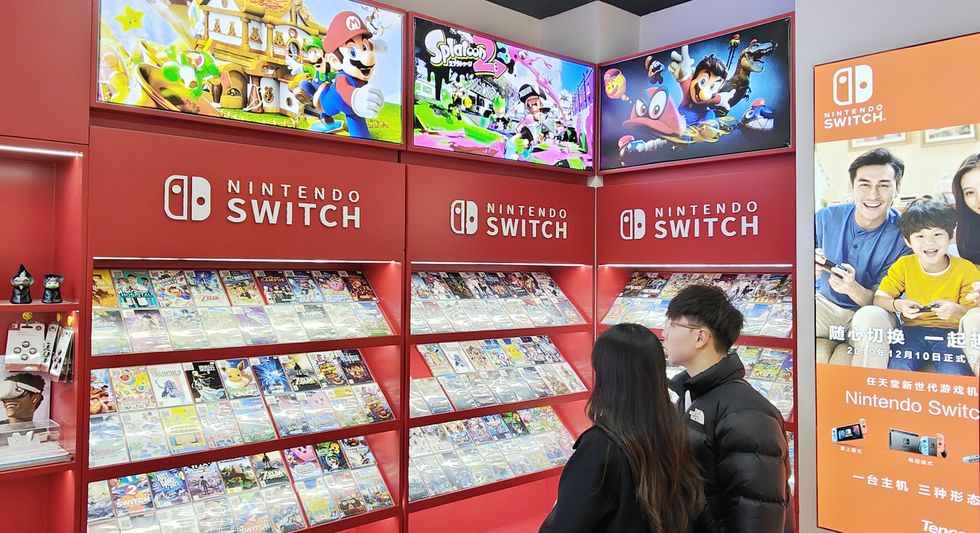 two people look at a shelf stacked with nintendo switch games and posters with characters like super mario and splatoon