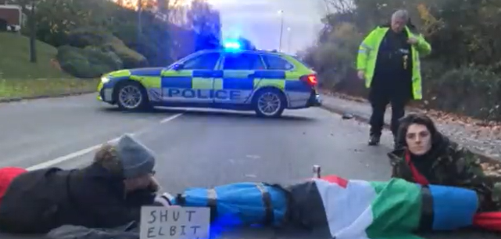 Two people lying in the road with a police car in the background