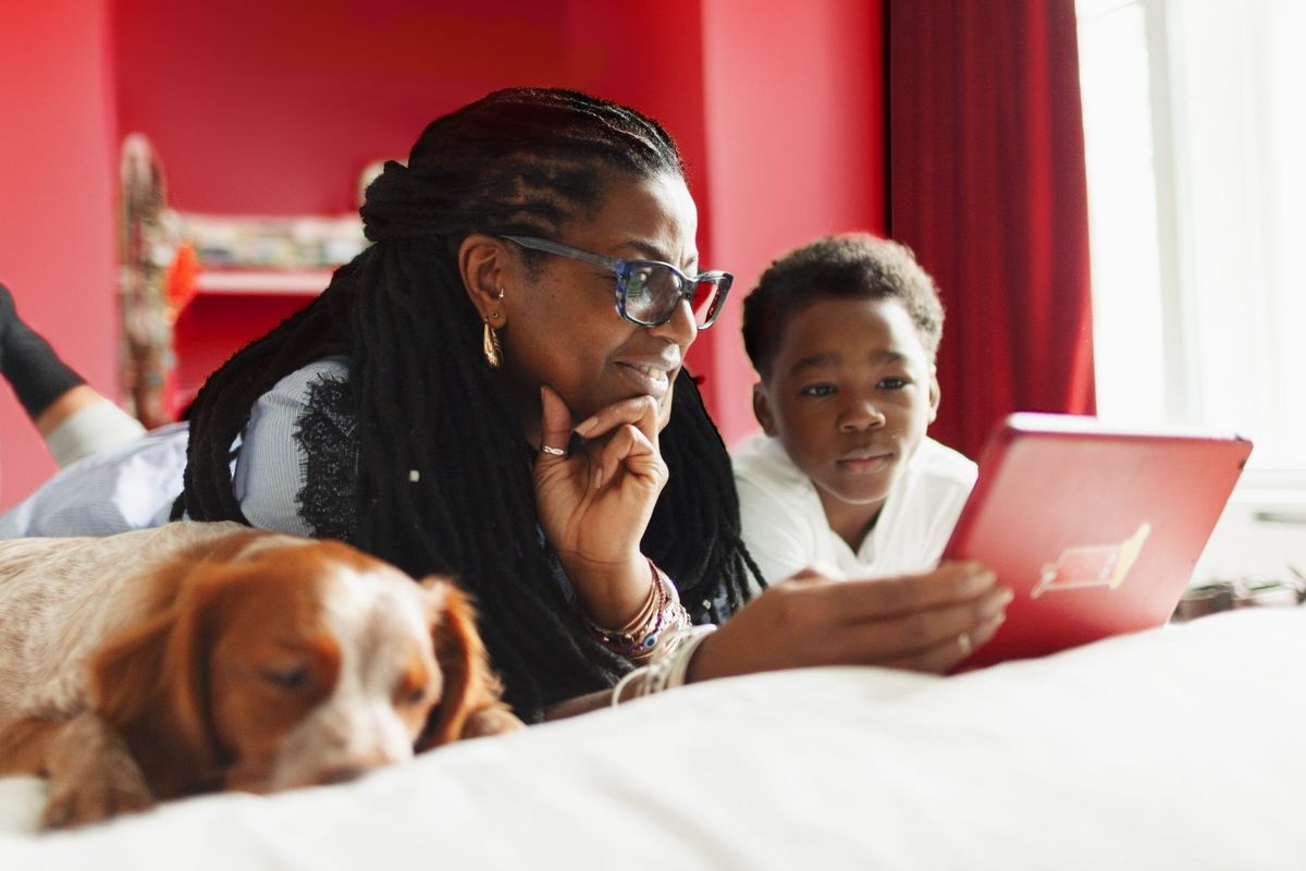 two people lying on a bed next to a dog using a tablet  