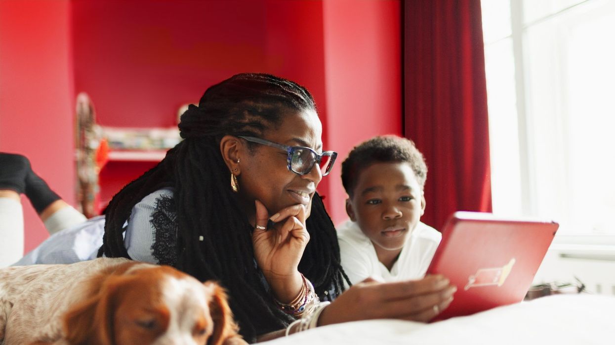 two people lying on a bed next to a dog using a tablet