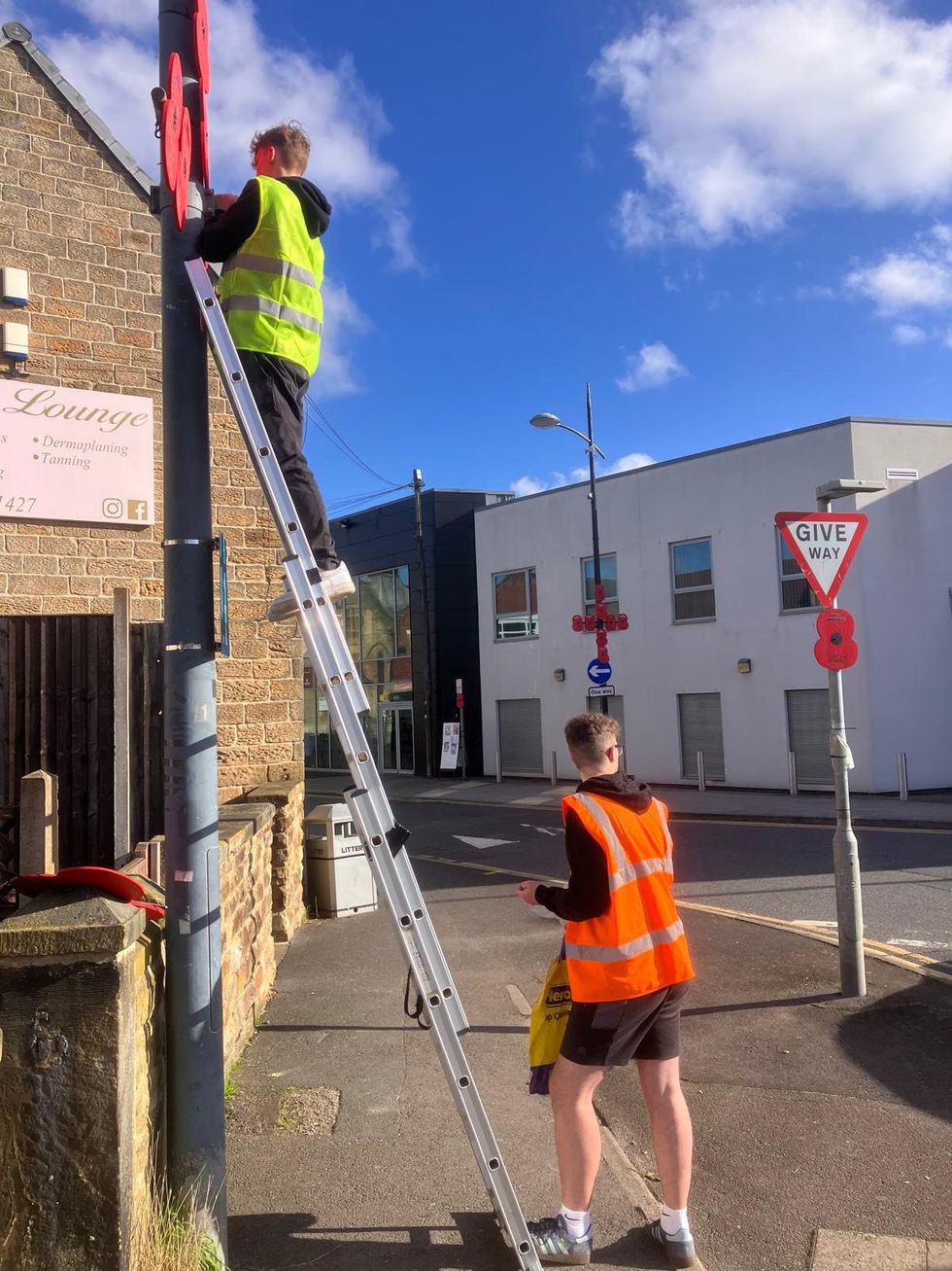 Two people putting a poppy display onto a lamppost