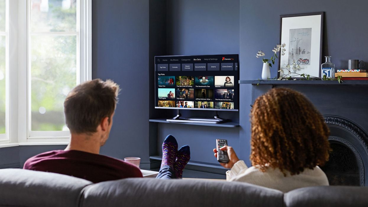 two people sit on a sofa watching a flatscreen television with the freeview menu on-screen