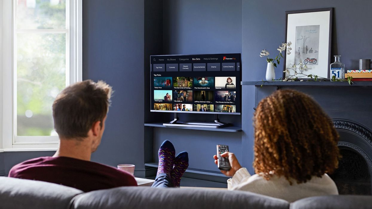 two people sit on a sofa watching a flatscreen television with the freeview menu on-screen