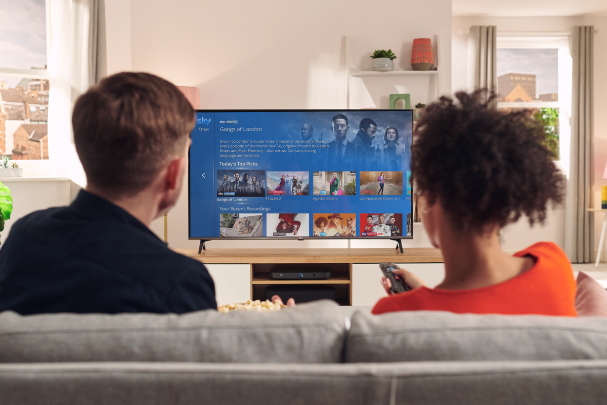 two people sit on a sofa watching sky tv on a flatscreen television