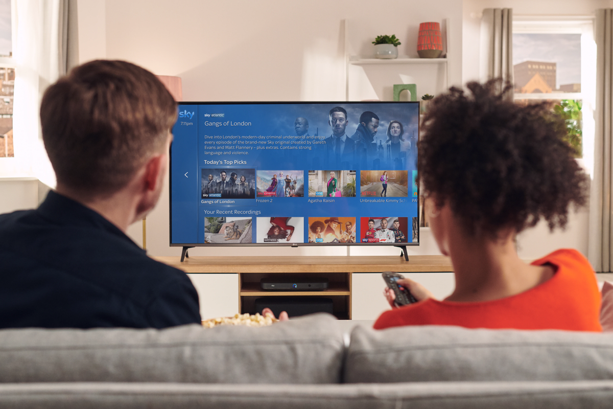 two people sit on a sofa watching sky tv on a flatscreen television 