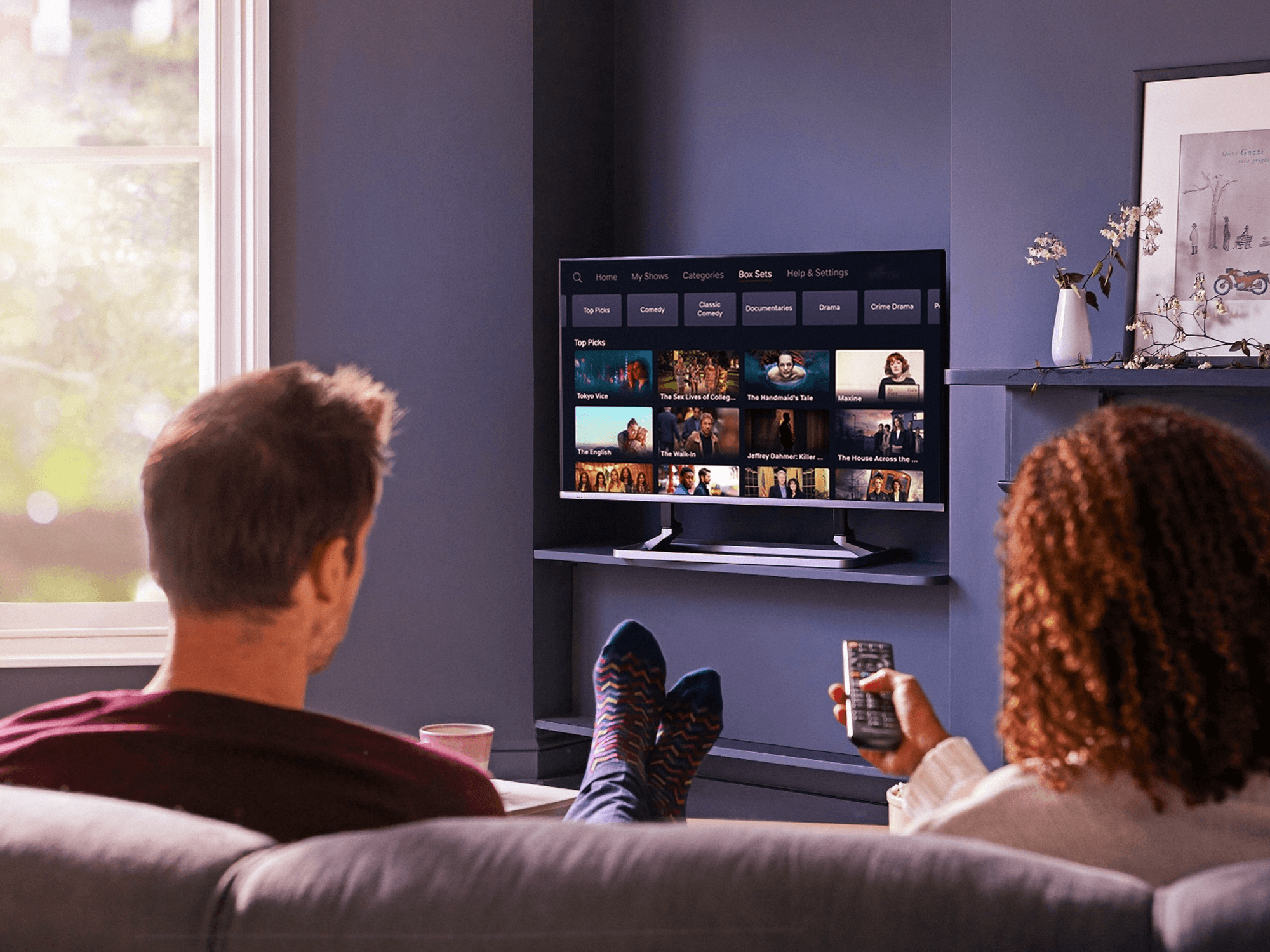 two people sit on a sofa with their feet on a table watching television on a smart tv powered by freely and freeview