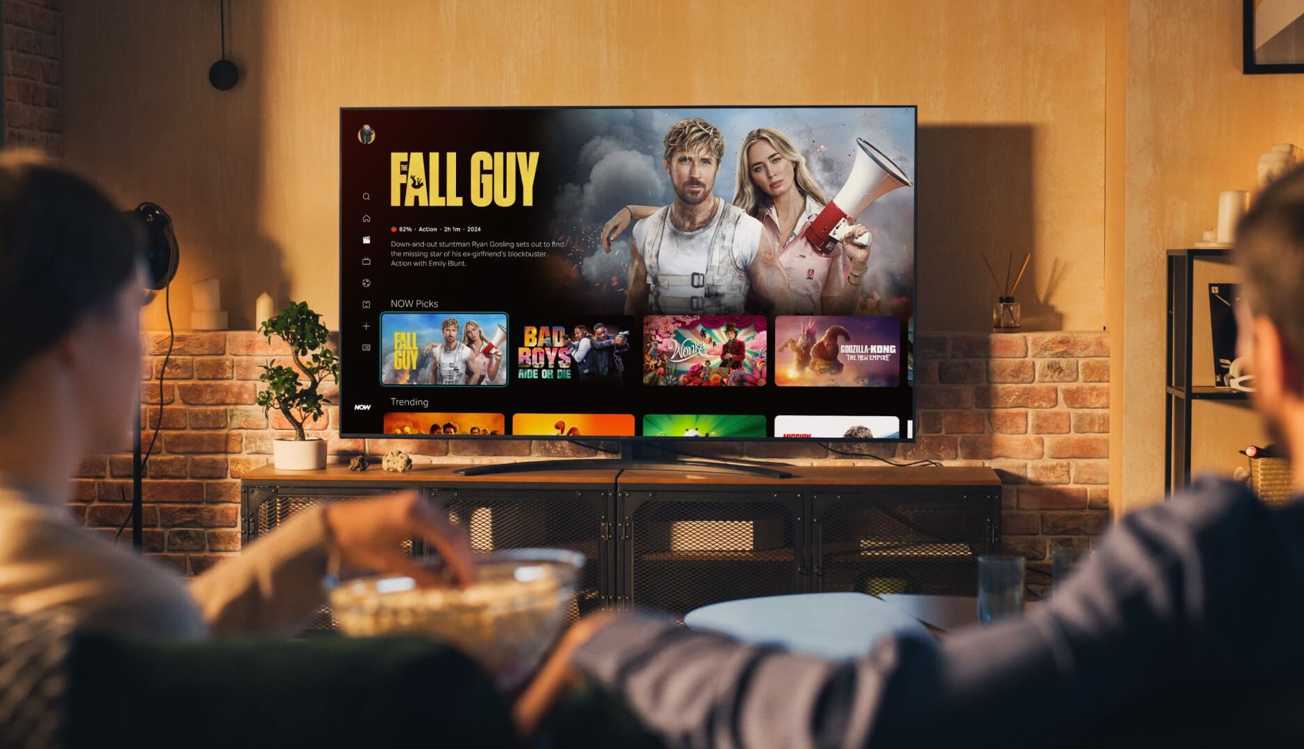 two people sitting on a sofa watching the new now app on tv