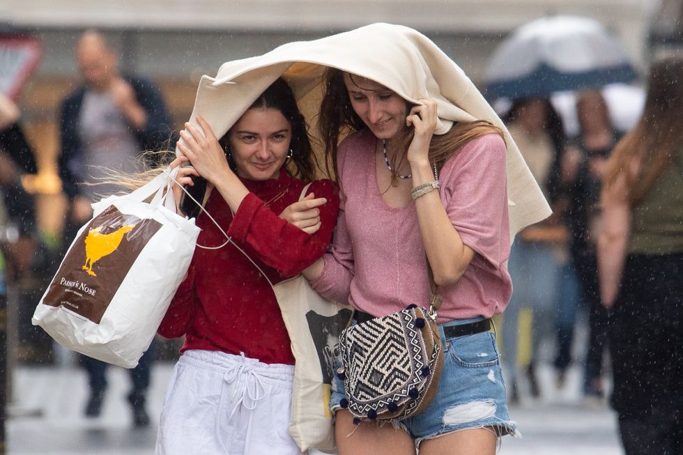 Two women take shelter under a coat during a sudden downpour of rain in Covent Garden, London, as parts of the UK are hit by heavy rain and thunderstorms. Picture date: Sunday July 4, 2021.